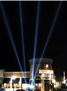 Four advertising searchlight beams over a store grand opening