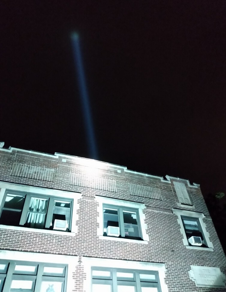Single-beam searchlight rental rising above a brick building in Evanston